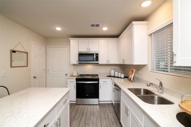 kitchen featuring white cabinetry, sink, light stone counters, light hardwood / wood-style floors, and appliances with stainless steel finishes