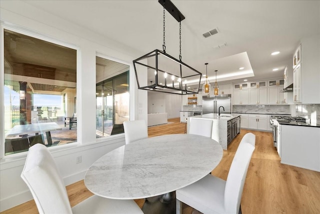 dining space featuring light hardwood / wood-style floors, a tray ceiling, and sink