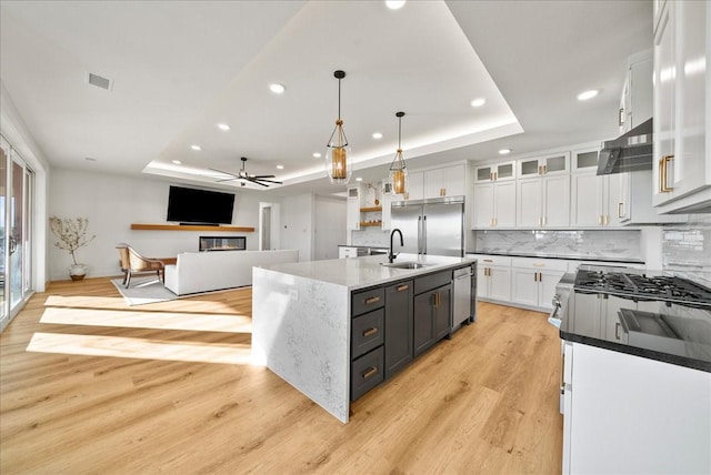 kitchen with pendant lighting, a raised ceiling, an island with sink, and white cabinets