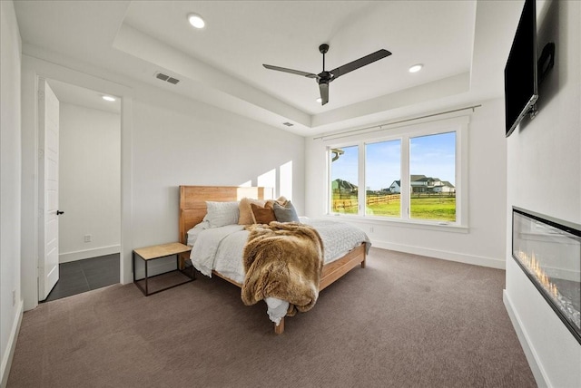 bedroom with dark colored carpet, ceiling fan, and a tray ceiling