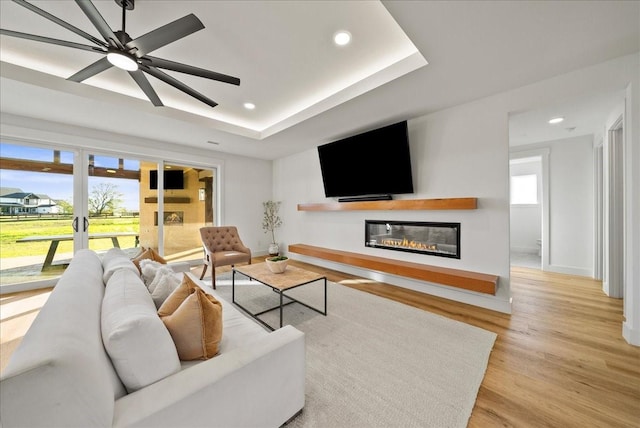 living room with a raised ceiling, plenty of natural light, light wood-type flooring, and french doors