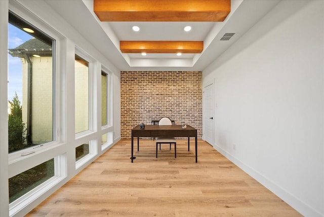 home office featuring beamed ceiling, light wood-type flooring, and brick wall