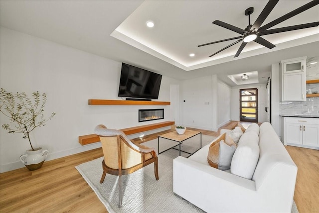 living room featuring light wood-type flooring, a raised ceiling, and ceiling fan