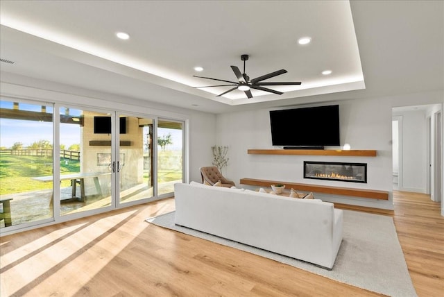 living room featuring a tray ceiling, ceiling fan, and light wood-type flooring