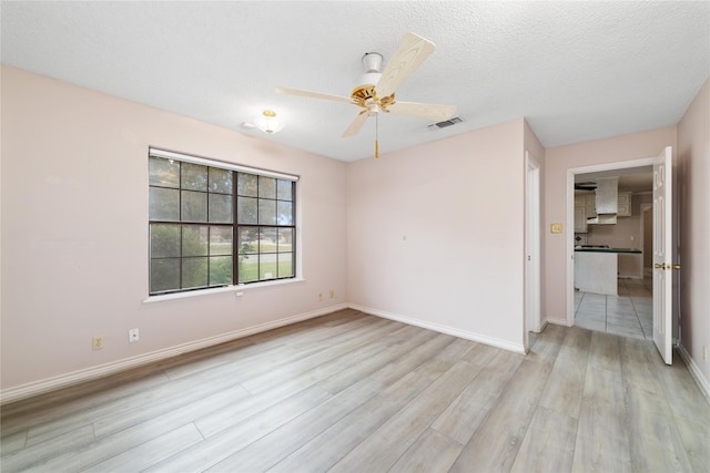 unfurnished room with ceiling fan, light wood-type flooring, and a textured ceiling