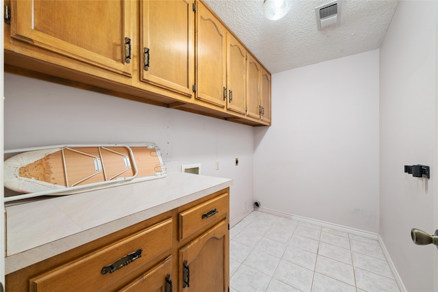 laundry area featuring cabinets, hookup for an electric dryer, hookup for a washing machine, a textured ceiling, and light tile patterned flooring