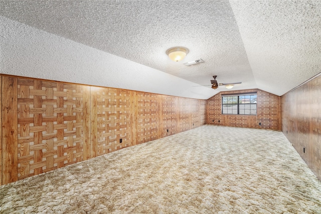 additional living space with carpet flooring, a textured ceiling, vaulted ceiling, ceiling fan, and wooden walls