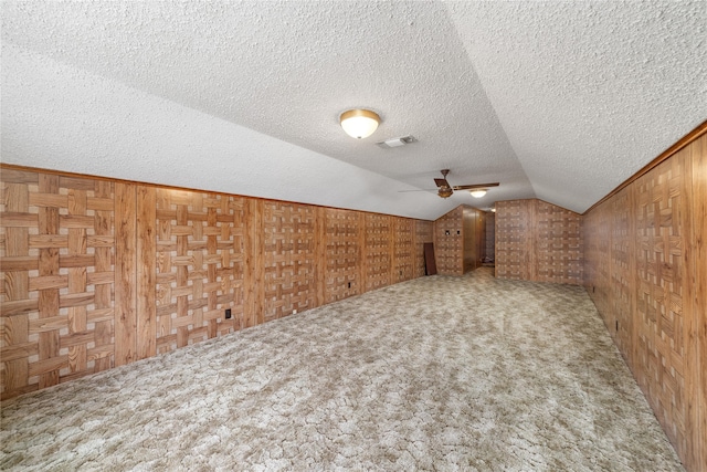 bonus room featuring lofted ceiling, a textured ceiling, carpet floors, and wooden walls