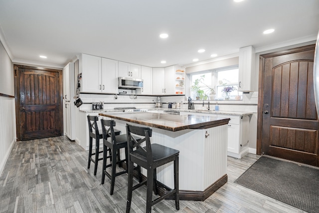 kitchen with a center island, light hardwood / wood-style flooring, a kitchen bar, decorative backsplash, and white cabinets