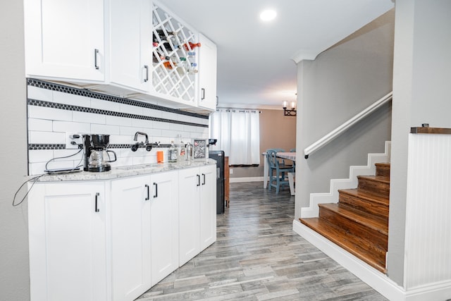 kitchen with backsplash, white cabinets, light hardwood / wood-style flooring, ornamental molding, and light stone countertops