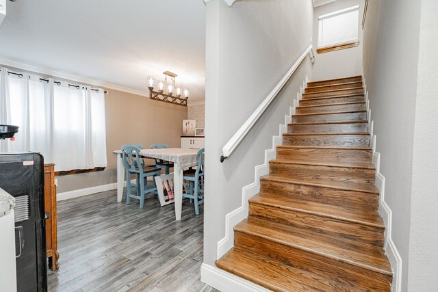 stairs featuring hardwood / wood-style floors, crown molding, and an inviting chandelier