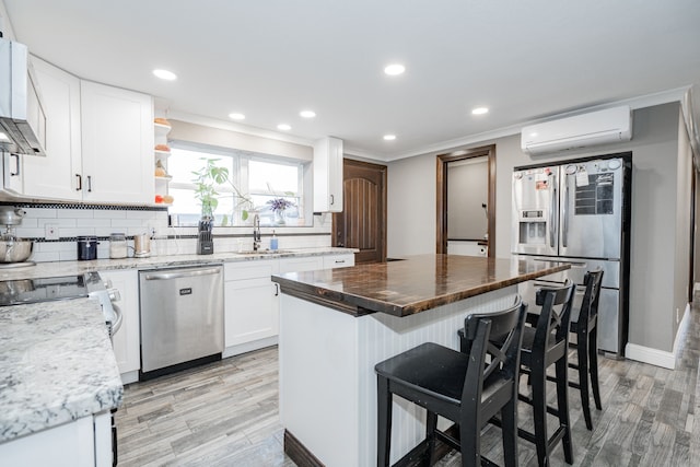 kitchen featuring stainless steel appliances, a wall mounted air conditioner, a kitchen island, white cabinets, and light wood-type flooring