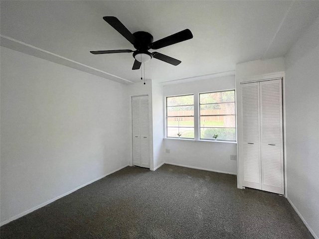 unfurnished bedroom featuring dark colored carpet, ceiling fan, and two closets