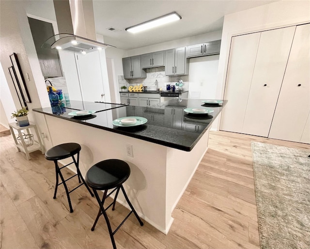 kitchen with gray cabinetry, a breakfast bar, light wood-type flooring, kitchen peninsula, and island exhaust hood