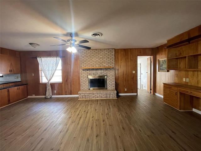 unfurnished living room featuring ceiling fan, a brick fireplace, wooden walls, and dark hardwood / wood-style flooring