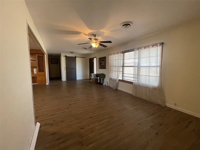 unfurnished living room with dark wood-type flooring, ceiling fan, and a barn door