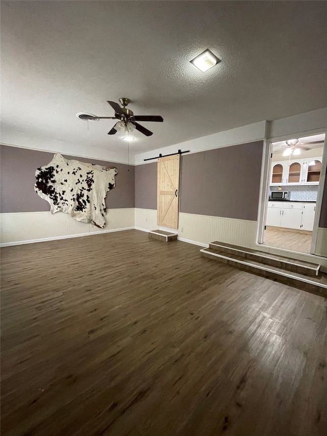 spare room featuring a textured ceiling, dark wood-type flooring, a barn door, and ceiling fan