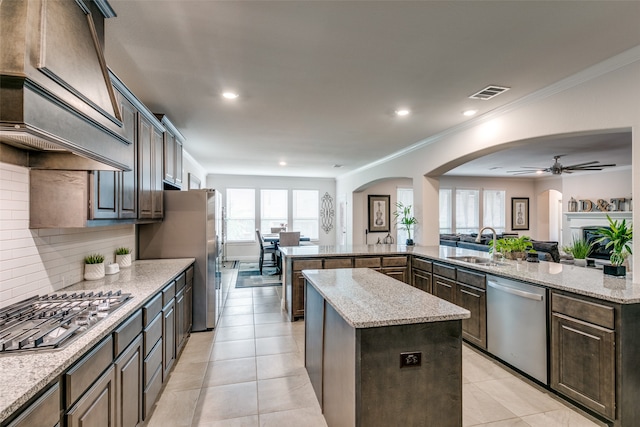 kitchen with dark brown cabinets, a kitchen island, light stone countertops, and stainless steel appliances