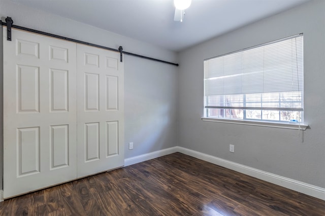 unfurnished bedroom featuring a barn door, ceiling fan, a closet, and dark hardwood / wood-style floors