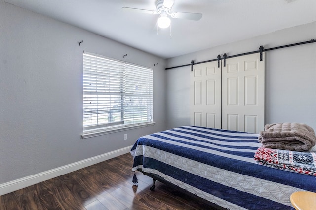 bedroom with ceiling fan, a barn door, and dark hardwood / wood-style floors