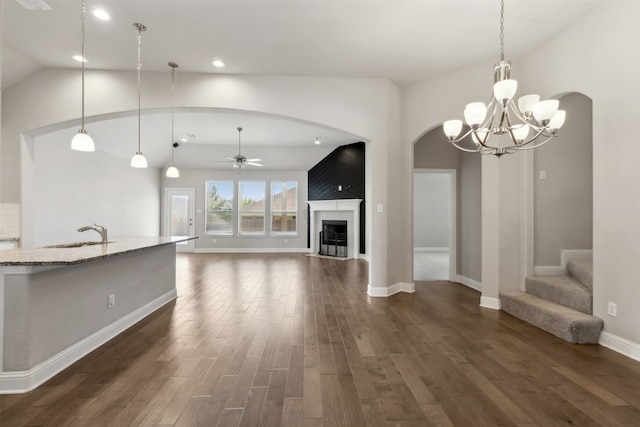 unfurnished living room with ceiling fan with notable chandelier, sink, a fireplace, dark hardwood / wood-style floors, and lofted ceiling