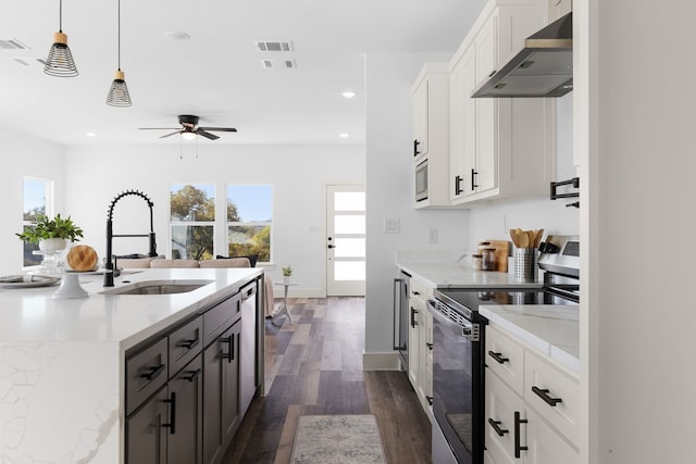 kitchen with hanging light fixtures, wall chimney exhaust hood, light stone counters, white cabinetry, and stainless steel appliances