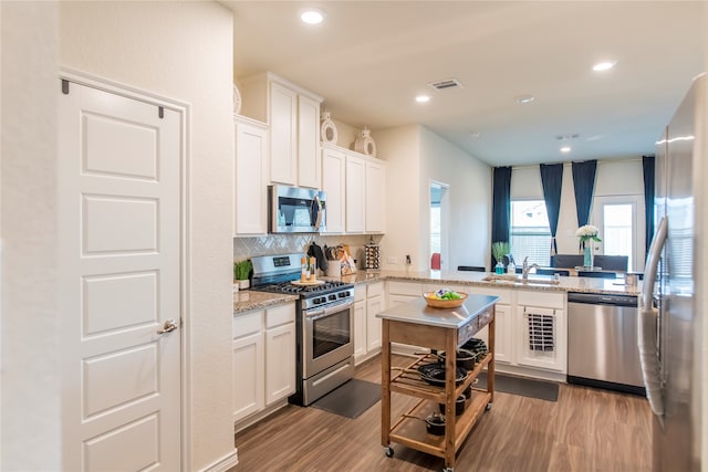 kitchen with light hardwood / wood-style floors, light stone countertops, white cabinetry, and appliances with stainless steel finishes