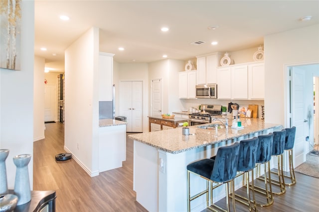 kitchen with white cabinets, appliances with stainless steel finishes, light hardwood / wood-style floors, kitchen peninsula, and a breakfast bar area