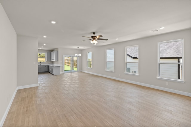 unfurnished living room featuring ceiling fan with notable chandelier and light wood-type flooring