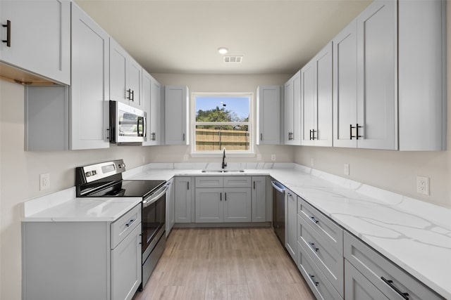 kitchen with gray cabinetry, sink, light hardwood / wood-style flooring, appliances with stainless steel finishes, and light stone counters