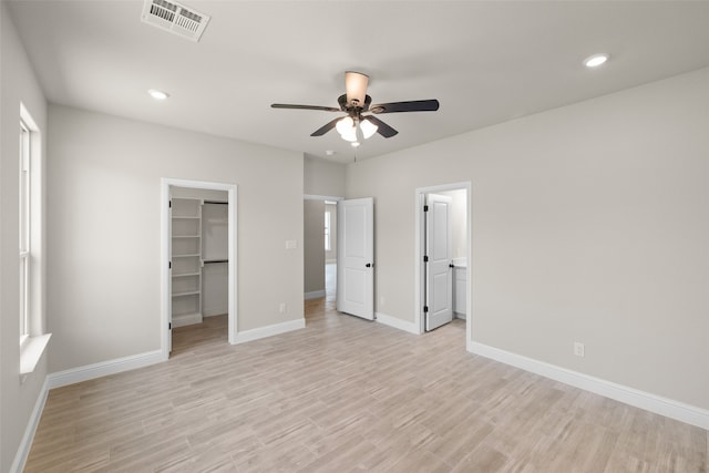 unfurnished bedroom with a walk in closet, ceiling fan, connected bathroom, light hardwood / wood-style floors, and a closet