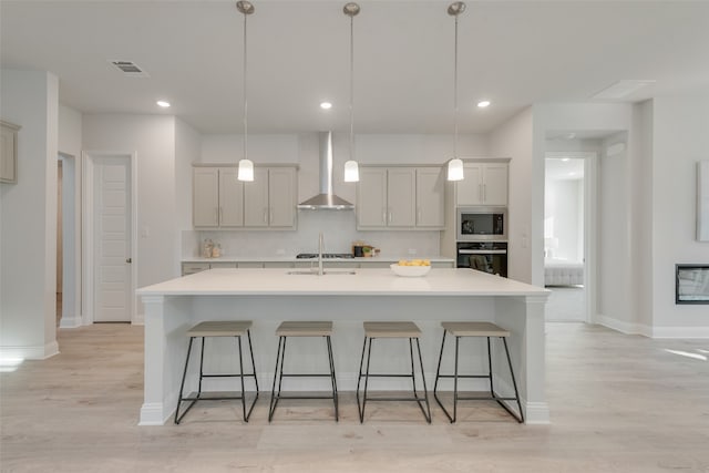 kitchen featuring pendant lighting, wall chimney exhaust hood, stainless steel appliances, and an island with sink