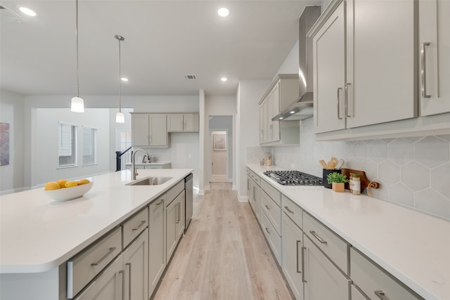 kitchen featuring appliances with stainless steel finishes, wall chimney range hood, sink, a center island with sink, and light hardwood / wood-style floors