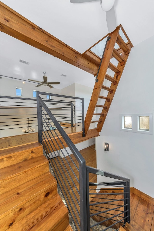 staircase with beamed ceiling, ceiling fan, and hardwood / wood-style floors