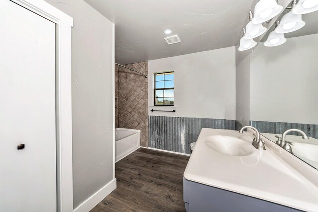 full bathroom featuring hardwood / wood-style floors, vanity, tiled shower / bath, toilet, and a notable chandelier