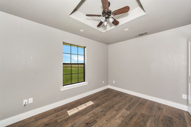 spare room with a tray ceiling, ceiling fan, and dark hardwood / wood-style flooring