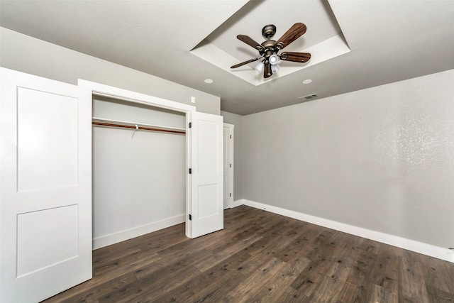 unfurnished bedroom featuring a raised ceiling, ceiling fan, a closet, and dark wood-type flooring