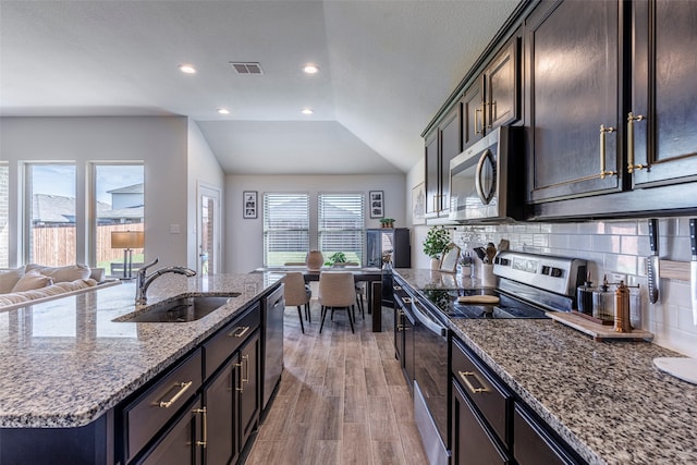 kitchen featuring lofted ceiling, sink, an island with sink, light hardwood / wood-style floors, and stainless steel appliances