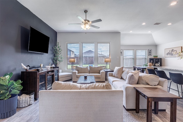 living room with ceiling fan, light hardwood / wood-style floors, and vaulted ceiling