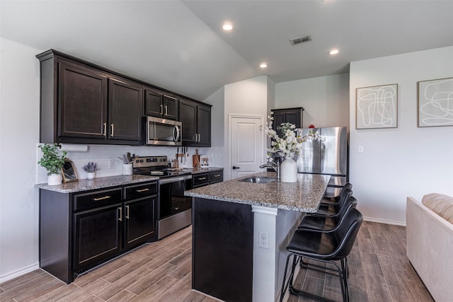 kitchen featuring light stone countertops, a kitchen breakfast bar, stainless steel appliances, light hardwood / wood-style flooring, and an island with sink