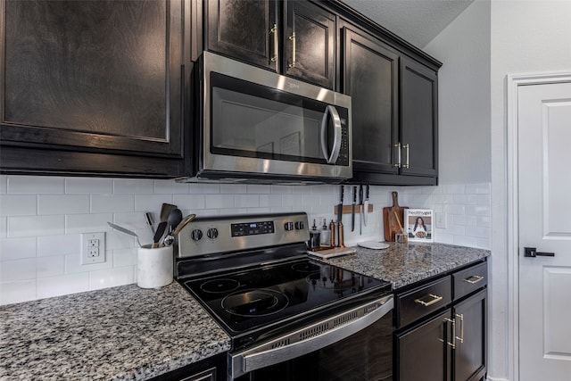 kitchen featuring dark brown cabinetry, decorative backsplash, dark stone counters, and appliances with stainless steel finishes