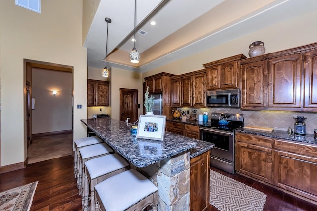 kitchen with dark stone counters, stainless steel appliances, dark wood-type flooring, decorative light fixtures, and a center island