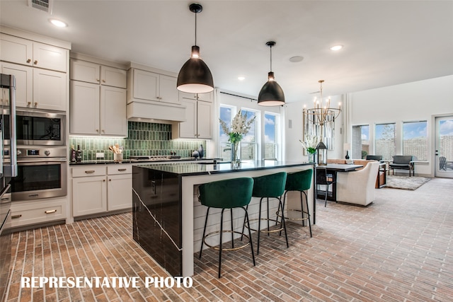 kitchen with tasteful backsplash, a wealth of natural light, stainless steel oven, and a center island with sink