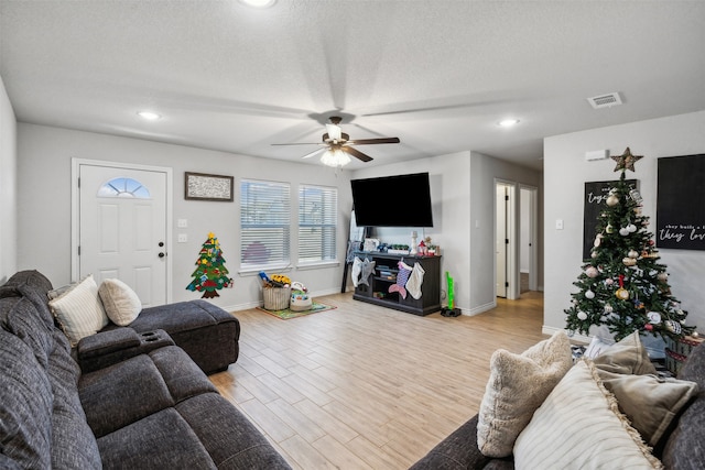 living room with ceiling fan, light wood-type flooring, and a textured ceiling