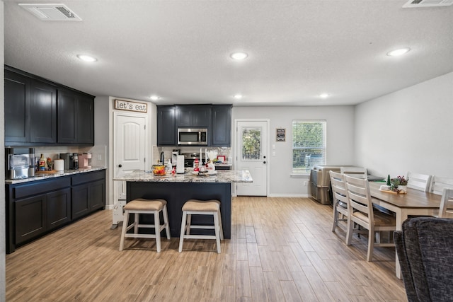 kitchen with a center island, light stone countertops, a textured ceiling, light hardwood / wood-style floors, and a breakfast bar area