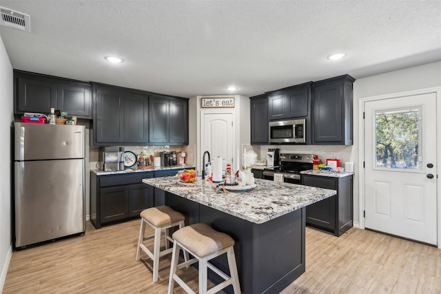 kitchen featuring a kitchen breakfast bar, light stone counters, light hardwood / wood-style floors, a center island with sink, and appliances with stainless steel finishes