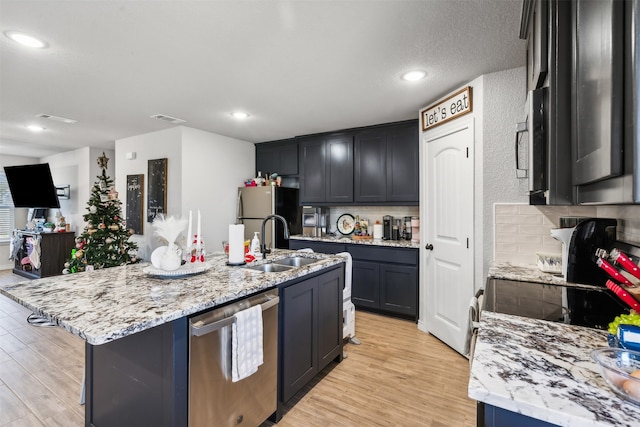 kitchen with appliances with stainless steel finishes, sink, light hardwood / wood-style flooring, and an island with sink