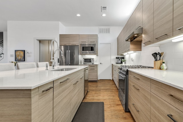 kitchen with sink, light brown cabinets, decorative backsplash, appliances with stainless steel finishes, and light wood-type flooring