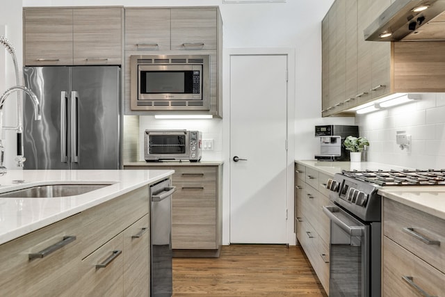 kitchen featuring hardwood / wood-style floors, light brown cabinets, exhaust hood, sink, and stainless steel appliances