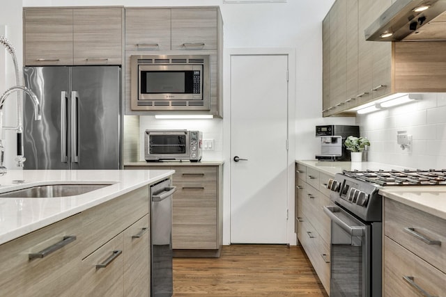 kitchen with appliances with stainless steel finishes, range hood, wood-type flooring, sink, and decorative backsplash